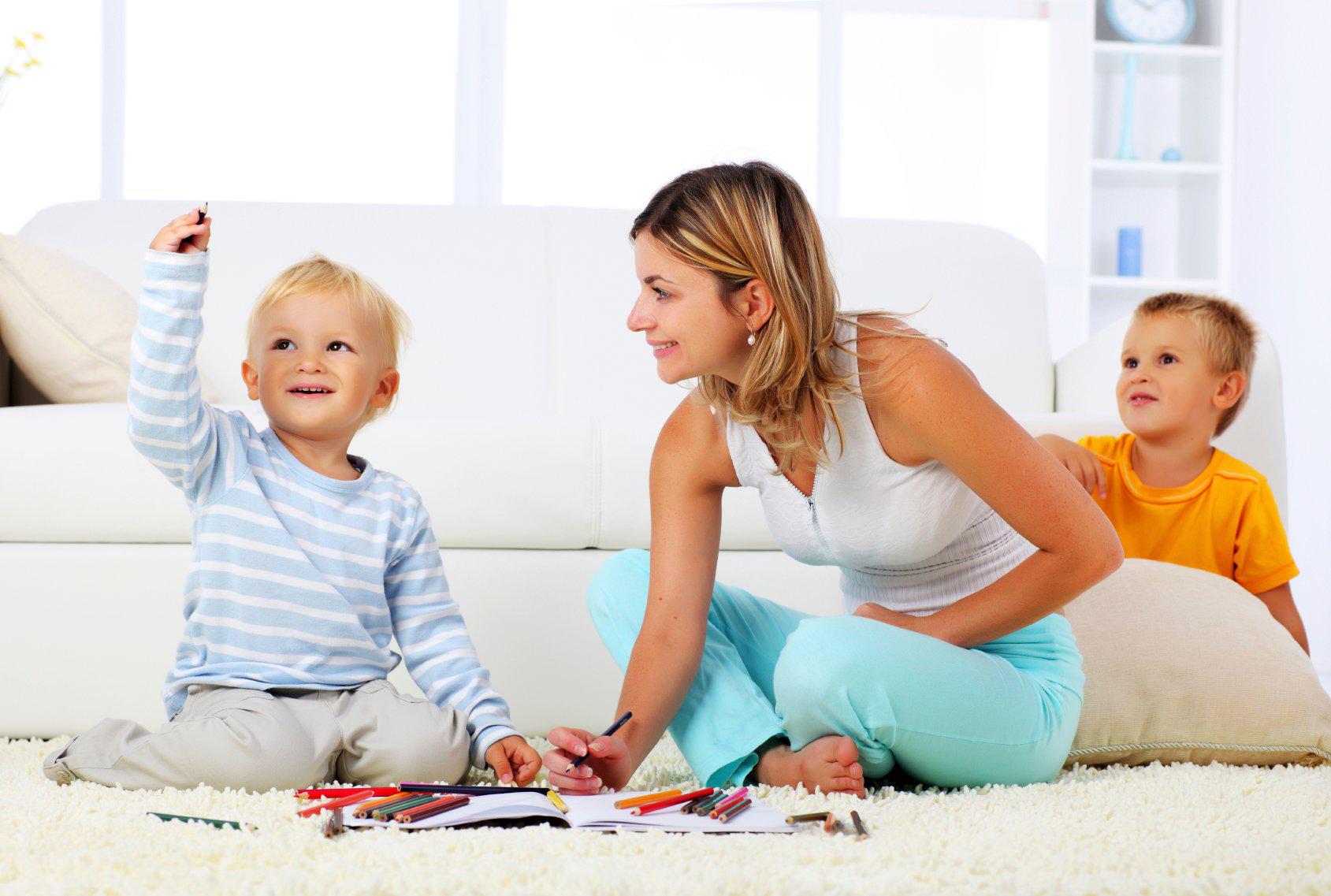 На фото ‒ мама с двумя детьми играет дома на ковре
