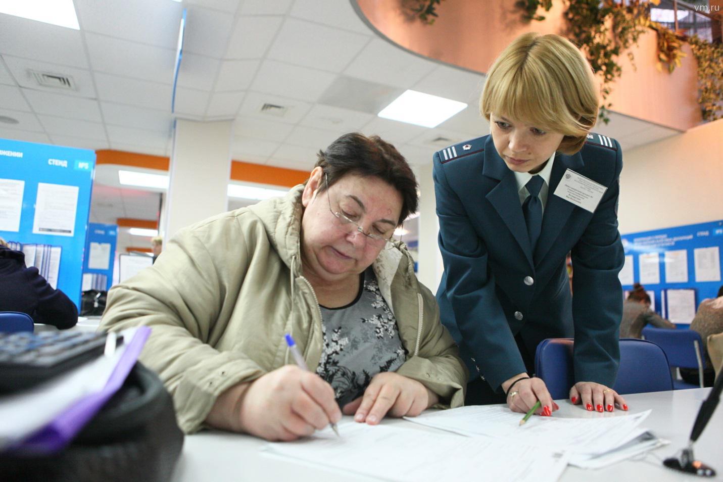 На фото ‒ Инспектор ФНС помогает человеку заполнять документы